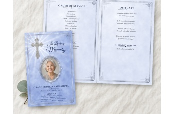 Bright Silver Cross bifold funeral program mockup on linen: the periwinkle blue cover, with a photo of a smiling older woman in a beaded silver oval frame under an engraved filigree silver cross, beside the open inside spread.